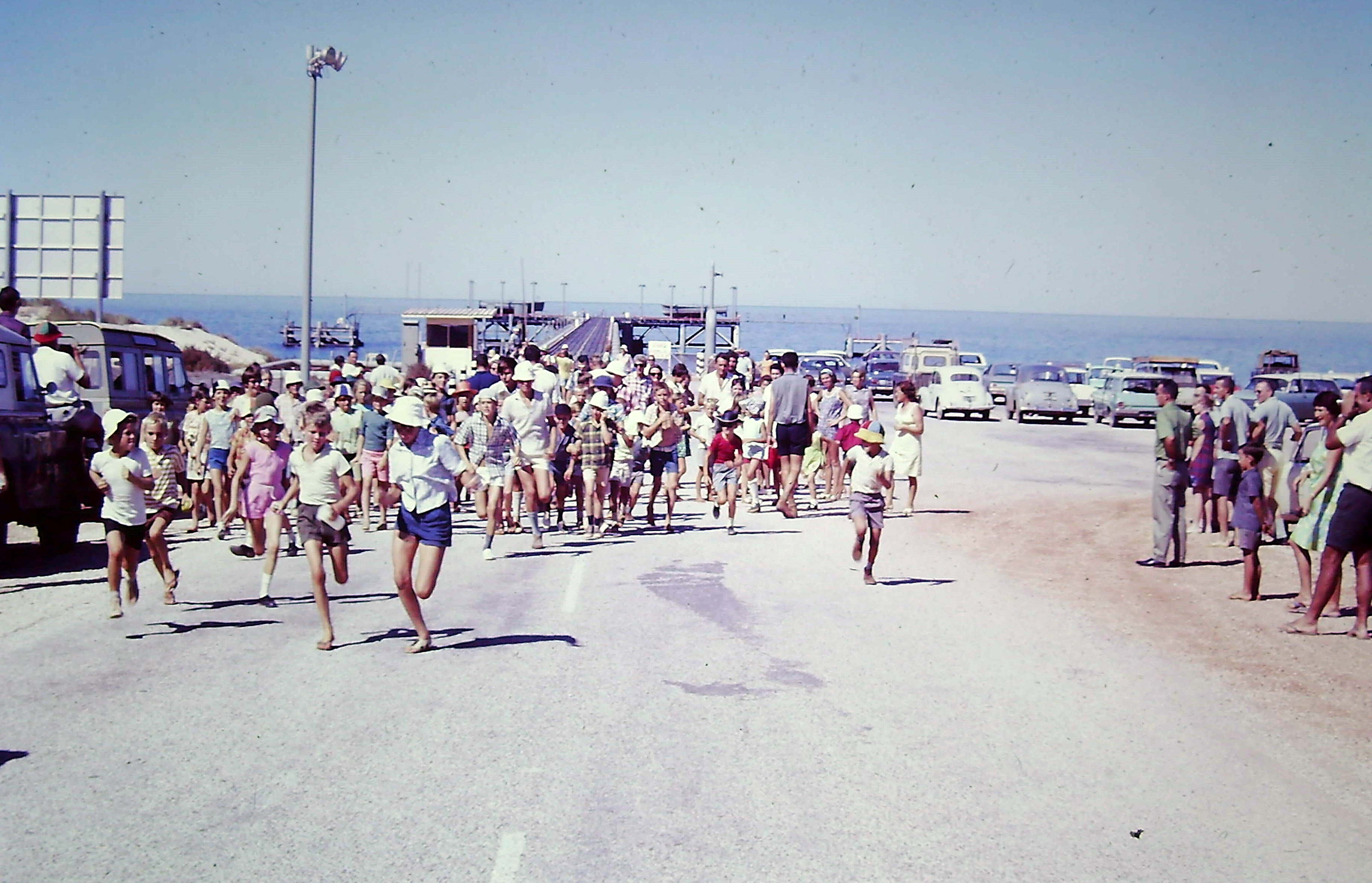 Group of kids running on a boat ramp. People having fun, two Land Rover Defenders parked.