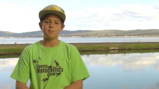 - Boy in Young Naturalists Club T-Shirt stand in front of a lake and hills