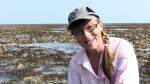 Sue Morrison crouched down on a reef talking to the camera  