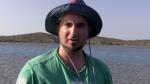 Andrew Cosgrove-Wilke talking to camera infront of a body of water wearing a hat  