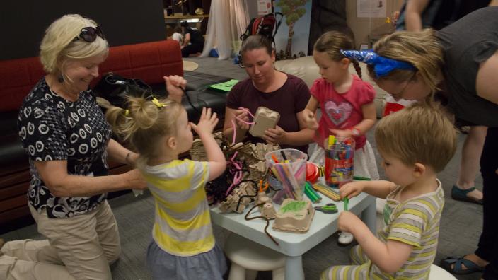 three toddlers and two adults sit around a table crafting