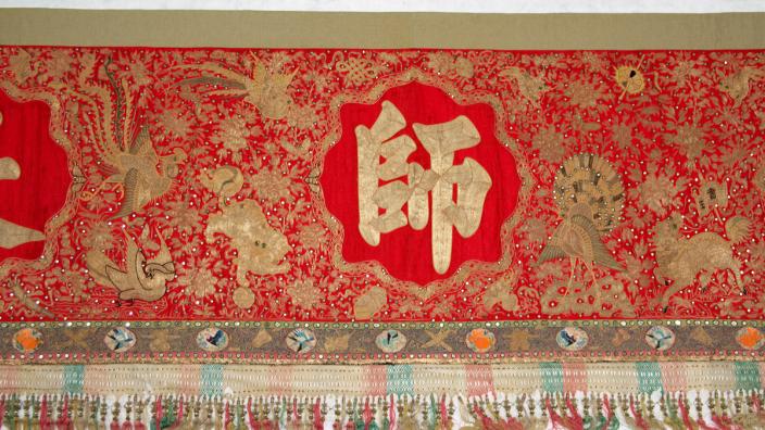The front of the banner is detailed with Chinese characters and motifs. a red banner with embroidered animals featuring Chinese text