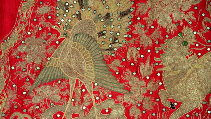 The red silk and blue stain banner details characters and motifs, including animals. embroidery of a golden peacock on red fabric