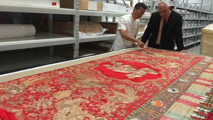 Two men stand over a table inspecting an embroidered banner