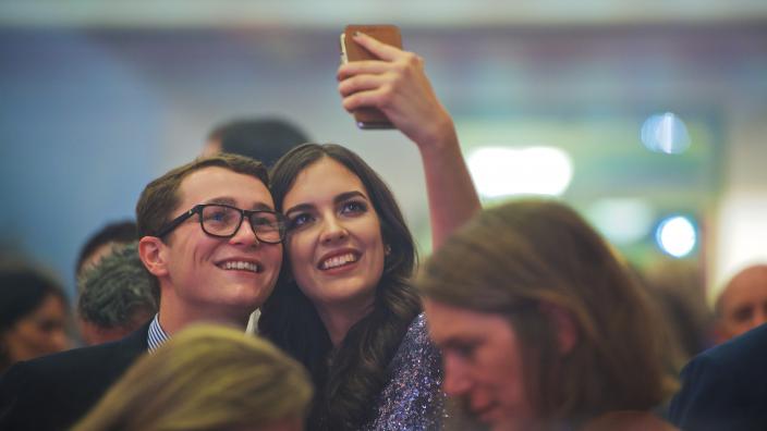 Caption: Pompeii After Dark Events (18+). "Two well-dressed people are stopped in a crowd, looking up to take a selfie."