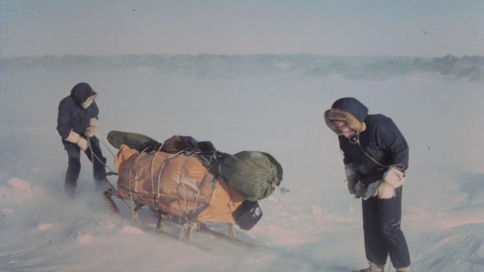 Two people dragging a heavy sled through thick snow and ice.