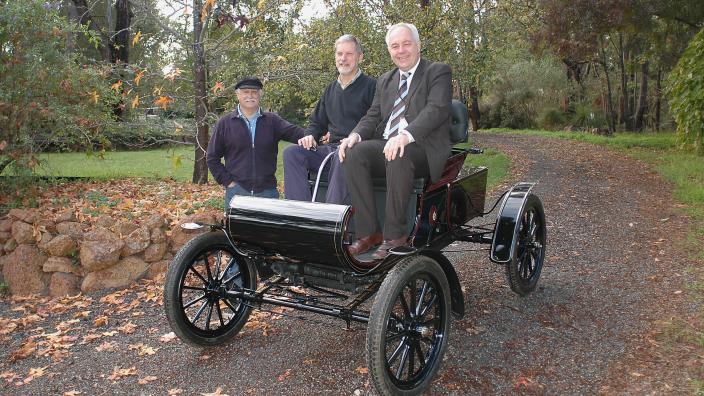 Two men seated in a fully restored turn-of-last century automobile