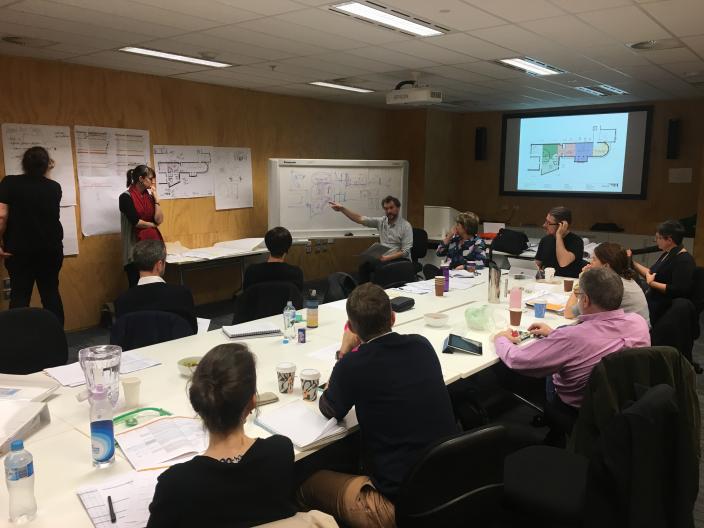 Room full of people sit in board room discussing while writing on whiteboard