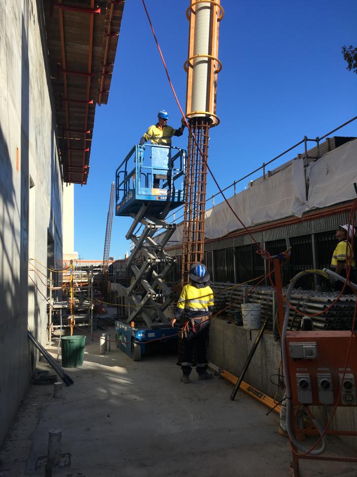 Worker on scissor lift guiding reinforced column to worker below