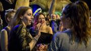 "A group of young women dressed to impressed laughing and having a drink. Two large dinosaur animatronics are in the background."