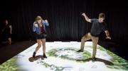 "Two young adults pretending to be dinosaurs are racing each other in a dinosaur trackway game."