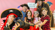 "A group of children and adults dressed as pirates, posing around a canon."