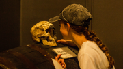 "A girl pressing her face against a replica skull of a pirate."