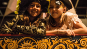 "Two girls dressed as pirates have their photo taken at the helm of a replica pirate ship."