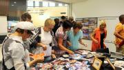 Room filled with people inspecting photographs laid out on a table in the middle of the Memory Room