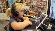 young child wearing headphones looks at school students work on an ipad