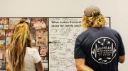 young man and woman look at photographs and comments on the wall left by visitors to the Memory Room