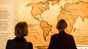 Two women looking at a large detailed map of the world.