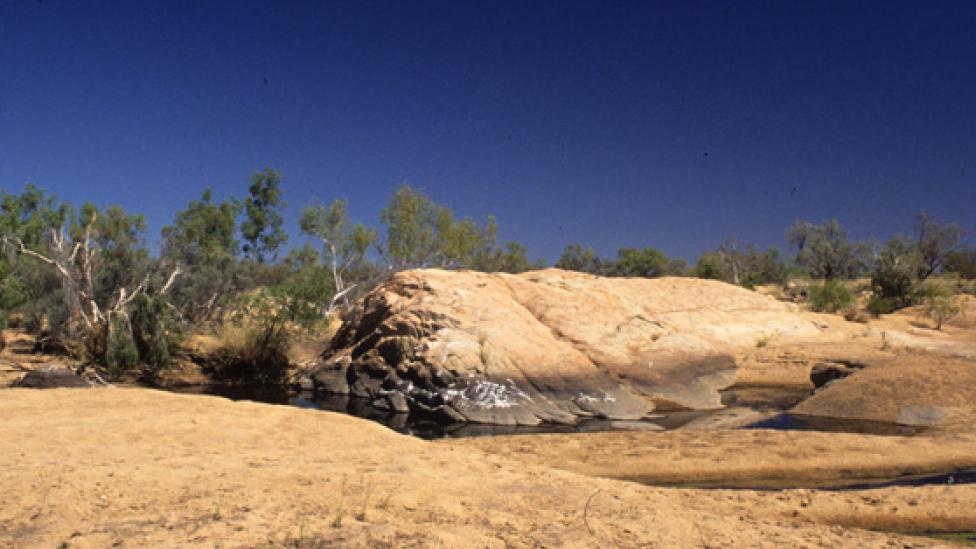 Rolling dry hard ground with small water oasis under a harsh hot sun