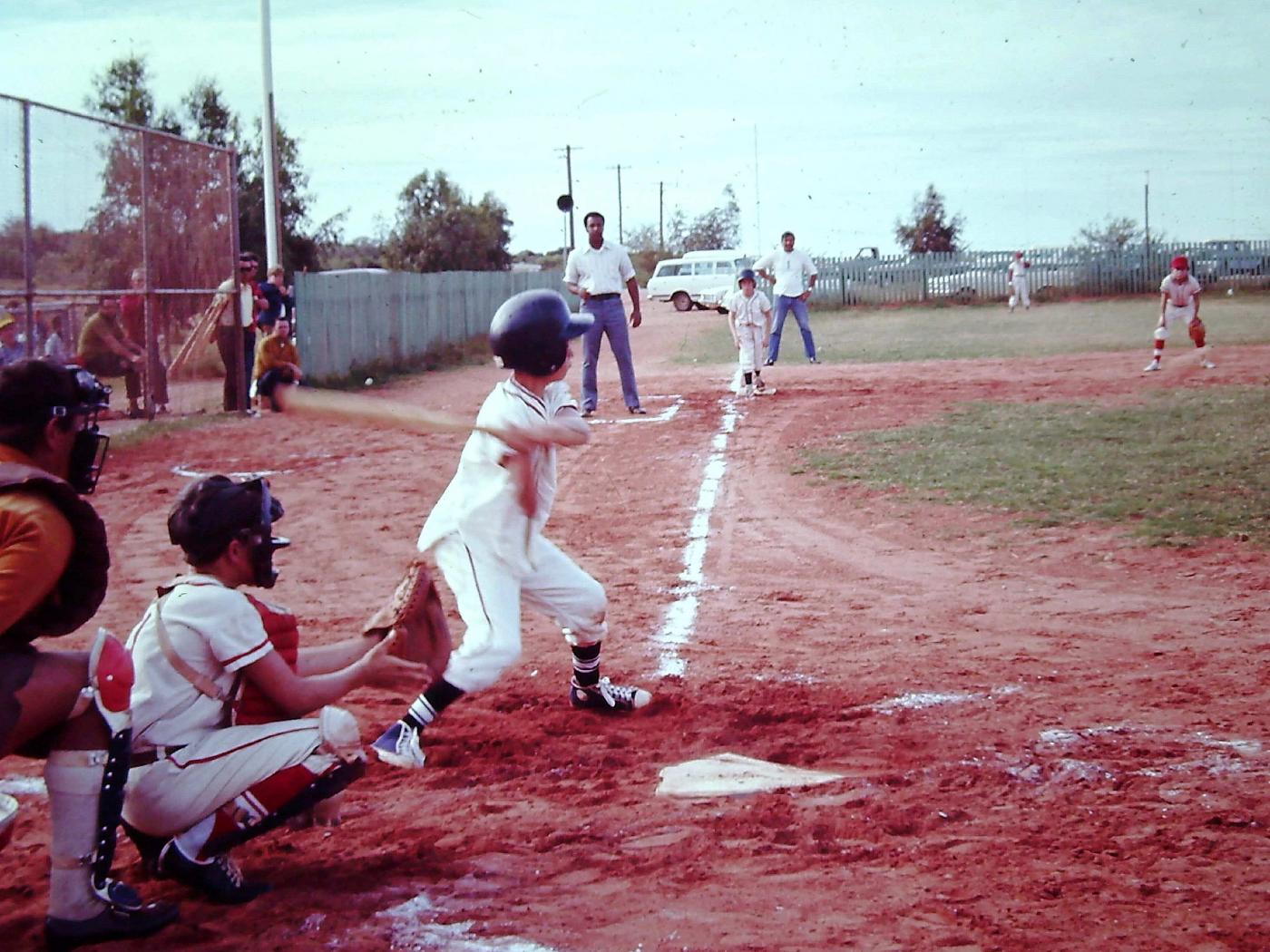 A young boy takes a swing at a baseball on a red dirt baseball park