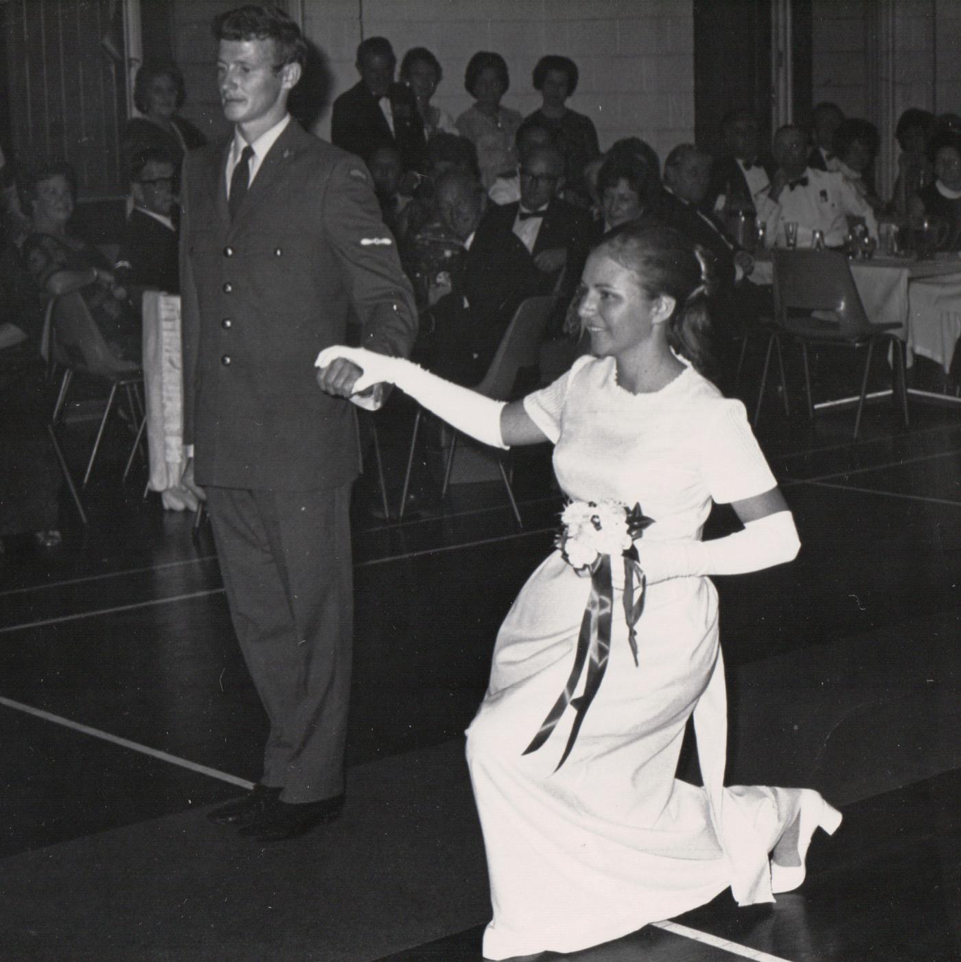 A young debutante curtsies while her partner holds her hand.