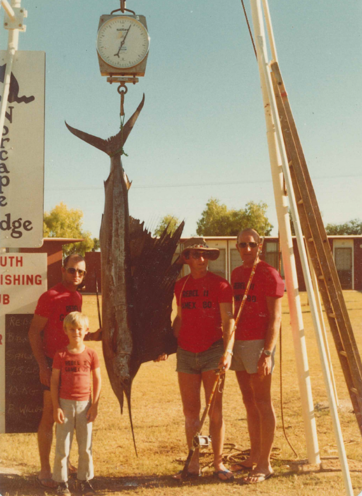 Three men and a young boy stand around a fish being weighed