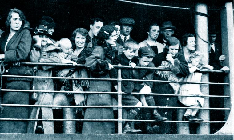 People standing shoulder to shoulder behind railings of a ship. 