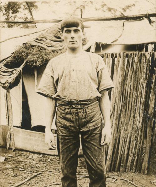 PHOTOGRAPH, B&W, postcard print, Matthew Harwood standing in front of improvised canvas, hessian and bush wood tent/ house, Canning Vale