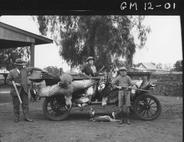 Picture of Turkey Shooting Party, with three people holding guns and showing off their catch on open car, 'Duff'