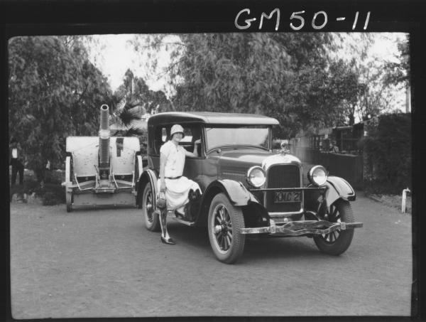 Miss Goldfields beside car in park large gun in background, Churack