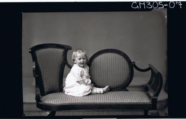 F/L Portrait of baby seated on lounge wearing lace dress; 'McCormack'