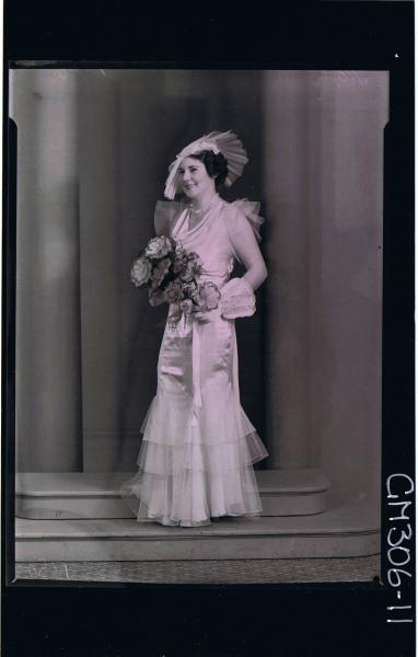 F/L Portrait of bride standing wearing long wedding dress,with 3 tiers,gloves with lace cuffs,holding bouquet 'Mohr' see 306-07