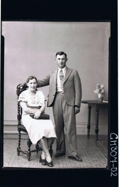 F/L Portrait of man standing wearing suit, woman seated wearing knee length dress, holding handbag; 'Masotti'