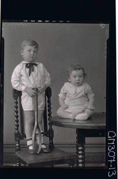 F/L Portrait of baby seated on table, small boy standing on chair wearing shirt, shorts, holding tennis racquet 'Stuber'