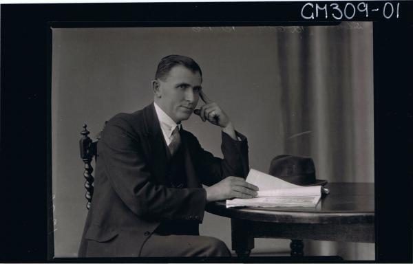 1/2 Portrait of man seated at table, wearing three piece suit, hat on table; 'Silverton'