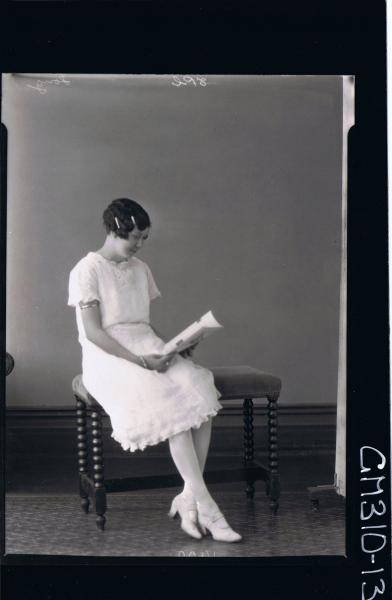 F/L Portrait of woman seated reading a book, wearing knee length lace dress; 'Song'