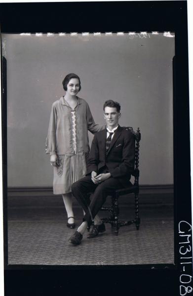 F/L Portrait of man seated wearing suit, woman standing wearing knee length day dress; 'McQuoid'