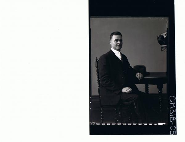 3/4 Portrait of man seated at table, wearing three piece suit, hat on table, 'O'Brien'