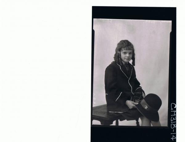 3/4 Portrait of girl seated wearing school uniform, holding hat with badge attached reads 'SACC' 'Stout'