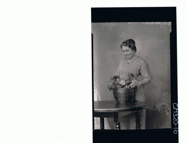 3/4 Portrait of woman standing behind a table, looking at basket of flowers wearing crochet dress 'Spargo'