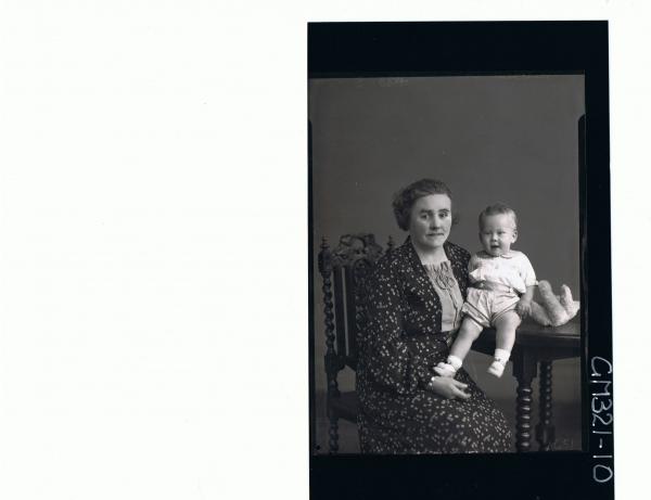 3/4 Portrait of woman seated wearing floral day dress, baby & teddy bear on table wearing shorts, shirt; 'Mitchell'