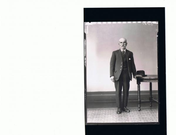 F/L Portrait of man standing wearing three piece suit, hat on table; 'Silver'