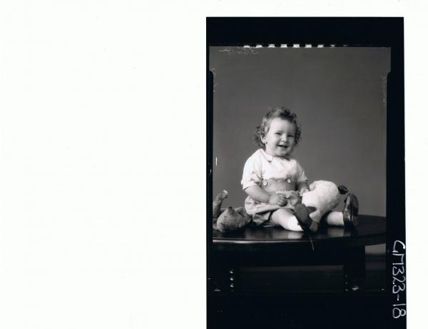 F/L Portrait of baby seated on table, wearing shorts, shirt and holding a toy dog, teddy bear lying on table; 'Smith'