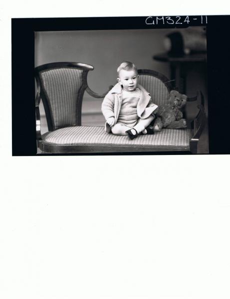 F/L Portrait of baby seated, wearing knitted shorts and top, jacket, teddy bear next to baby; 'Leggert'