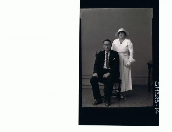 F/L Portrait of man seated wearing suit, spectacles, woman standing wearing 3/4 length dress, gloves and hat; 'Locke'