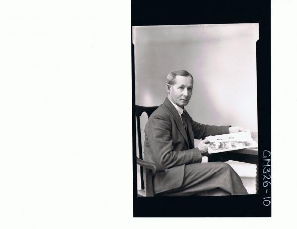 3/4 Portrait of man seated at table wearing suit holding a book; 'Moore'