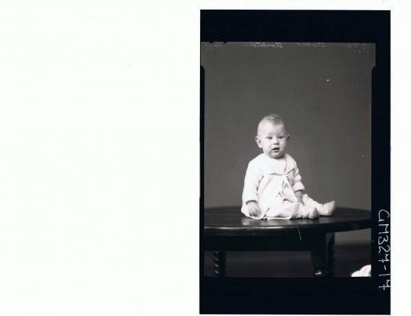 F/L Portrait of baby seated on table wearing lace dress, booties, knitted jacket; 'Stoker'