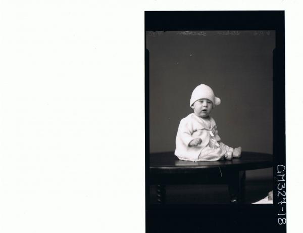 F/L Portrait of baby seated on table wearing lace dress, booties, knitted jacket; 'Stoker'