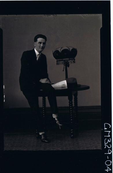 F/L Portrait of man seated on table wearing 3 piece suit, hat on table; 'Manley'