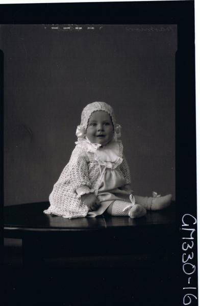 F/L Portrait of baby seated on table wearing dress, bib, cardigan, bonnet, booties; 'Marmion'